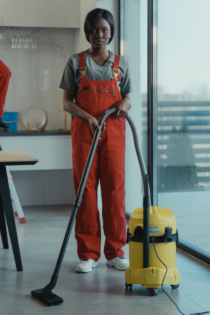 Une femme adulte vêtue d'une combinaison rouge utilise un aspirateur dans un intérieur moderne, en se concentrant sur les tâches de nettoyage.